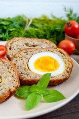 Meat cutlet with boiled egg, pieces on a ceramic plate on a dark wooden background. Mini meat rolls. Scottish cutlet.