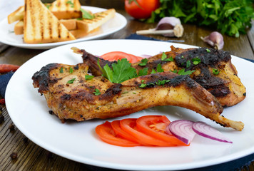 Fried rabbit legs on a white plate on a wooden table. Dietary rabbit meat cooked on the grill.