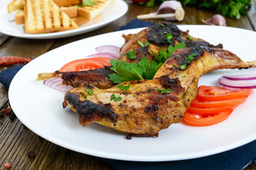 Fried rabbit legs on a white plate on a wooden table. Dietary rabbit meat cooked on the grill.