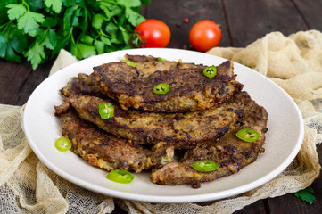 Pieces of fried pork liver on a plate on a dark wooden background.