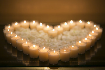 Heart created by combination of candles with white petals in the center. Romantic mood.