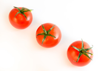Three small cherry tomatoes with stems arranged diagonally isolated on white tabletop background surface, top view
