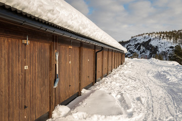 Brown gargae building, snow on the ground, mountains and white clouds on blue sky