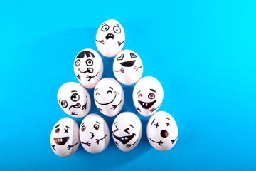 Easter eggs with different funny faces on blue background with copy space. Top view.