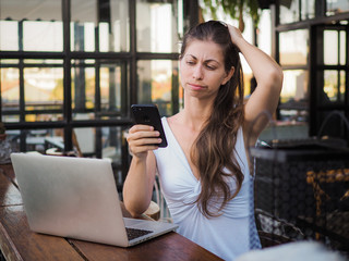 worrying and stressed digital nomad woman with laptop and phone at an outdoor coffee shop