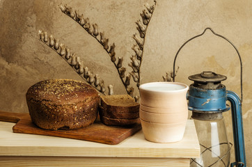 Milk in a ceramic pot, rye bread and a kerosene lantern. Still-life in the rustic style