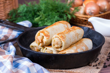 Crepes stuffed with minced meat and rice in a frying pan on a wooden table