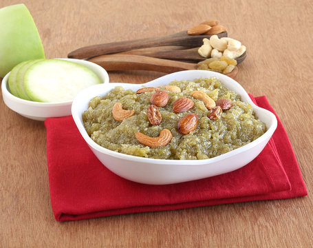 Lauki halwa, also known as doodhi, ghiya, or bottle gourd halwa, is a traditional and popular Indian sweet dish, on a wooden background with some of its main ingredients.