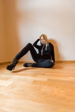 A beautiful young woman sitting on the floor and wearing black clothes.