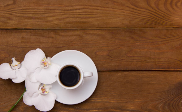 Cup Of Coffee And White Orchid Flowers On A Wooden Brown Table