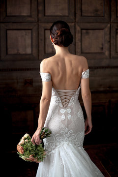 Elegance bride in sexy dress with open back holding bouquet in bark interior studio.Rear view.