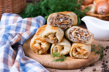 Crepes stuffed with minced meat and rice on a cutting board on a wooden table