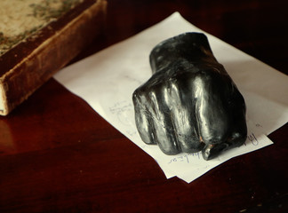black paper weight fist-shaped on hand written paper sheets, front view with soft focus