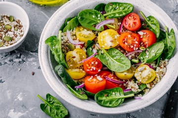 Healthy green bowl salad with spinach, quinoa, yellow and red tomatoes, onions and seeds