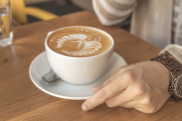 Girl holding espresso cup cappuccino in a cafe on a wooden table