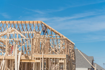 Rear view roofer builder worker with carpenter tool belt working on the roofing of new, two story residential home. Wood frame house under construction near completed houses, blue sky