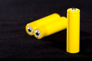 Three yellow batteries close-up on a dark black blurred background. Electrics. Battery power.  Accumulator on the fabric with villi. Space for text.