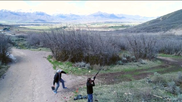 Aerial shot as men shoot a 12 guage shotgun at a clay pigeons