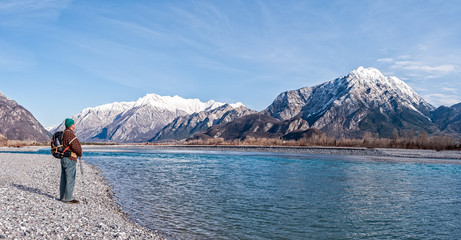 Man hiker on shore of river looking the mountains.