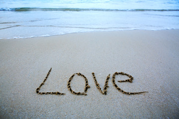 Word Love written on the sand near the sea.