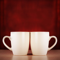 Two bright cups on a wooden surface on a dark red background