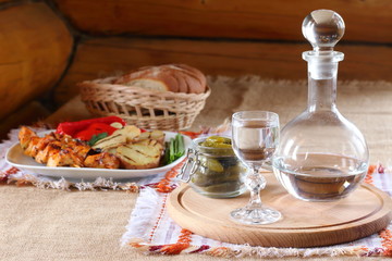 A glass of vodka and a hot snack on the table. A glass of vodka and a plate of chicken kebabs, grilled potatoes and vegetables.