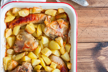 Baked potatoes with sausages and chicken in enameled form on a wooden table, top view, horizontal