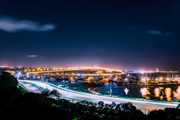cars in motion on a lighted bridge and highway over the sea with anchored sailing boats in a marina...