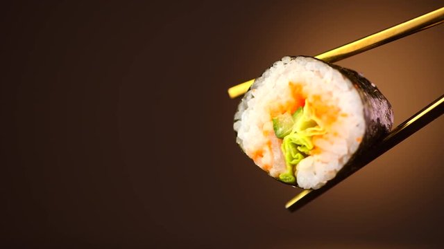 Sushi roll in chopsticks over black background. Seafood. Healthy eating, dieting concept. 4K UHD video footage. 3840X2160