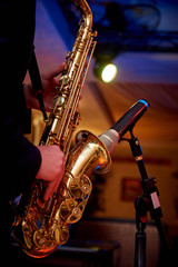 A golden saxophone in the hands of a musician near the microphone on the counter