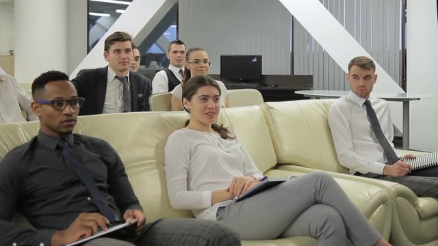 Multiethnical group of businesspeople is participating in the professional training. Causacian woman is rasing her hand and asking the question and her male and female colleagues sitting near on the