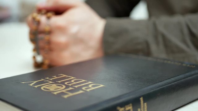 Holy bible on the table. Sunday Bible reading in church. Man praying holds in hand wooden rosary with cross