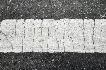 Close up picture of an asphalt road with a cracked white lane marking.