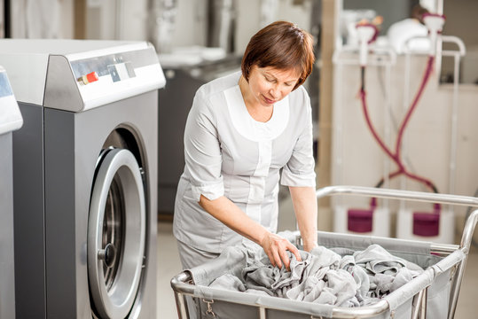 Senior washwoman in uniform working with towels standing near the wahing machine in the professional hotel laundry