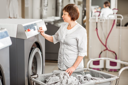 Senior washwoman in uniform working with washing machine in the professional hotel laundry