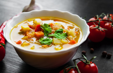 Bowl of chicken soup with vegetables on a dark wooden background