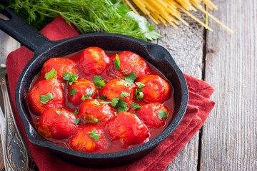 Meatballs in tomato sauce in a cast-iron frying pan on a wooden table, horizontal, copy space