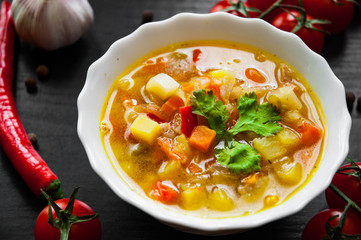 Bowl of chicken soup with vegetables on a dark wooden background