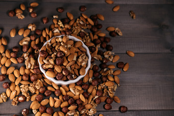 The white cup is filled with nuts. Nuts scattered around, hazelnuts, walnuts and almonds. View from above