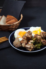 fried beef slices on a plate with fried egg. menu restaurant recipe concept . on a dark background