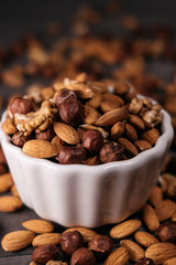 The white cup is filled with nuts. Nuts scattered around, hazelnuts, walnuts and almonds. Vertical frame