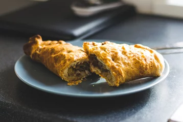 Cornish pasty cut in half on a blue pastel plate on the kitchen counter © Sean