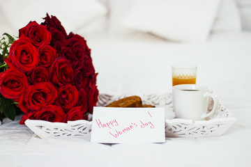 Breakfast in bed, celebrate valentines day, womens day or birthday. White bed, large bouquet of red roses. In the background of a pillow, a bedside table unfocus. copy space, free space.