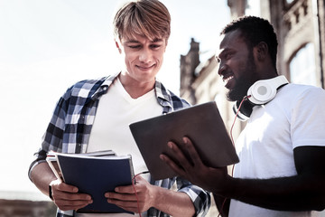 Digital technology. Positive nice cheerful afro American man holding a tablet and smiling while studying together with his friend