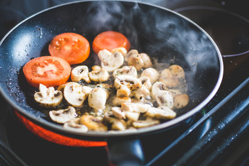 Tomatoes and mushrooms being fried in a black frying pan on an electric stove