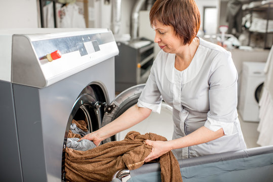 Senior washwoman taking of cleaned up towels from the washing machine in the laundry