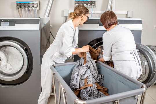 Two washwomen taking of cleaned up towels from the washing machine in the laundry