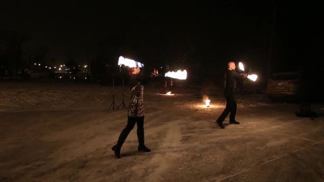 Amazing tribal fire show dance at night on winter under falling snow. Dance group performs with torch lights and pyrotechnics on snowy weather.