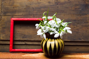 Snowdrop flowers in a vase on rustic wooden background