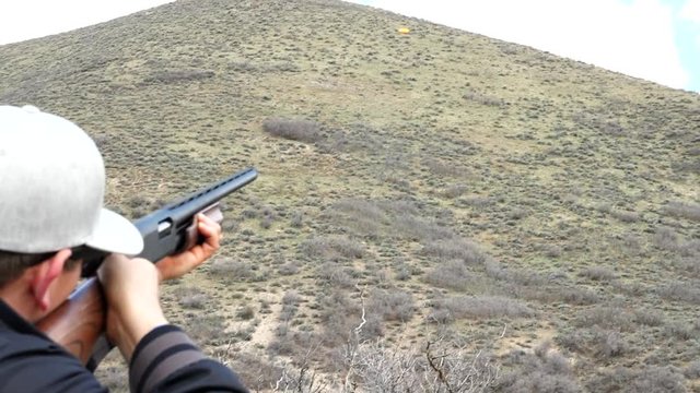 Slow motion man shoots clay pigeon with shotgun